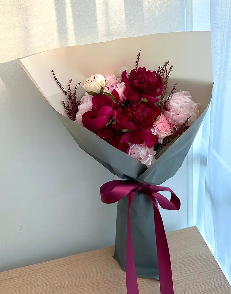 A395 red and pink peonies with light pink carnations, underlaid with soft khaki paper, wrapped in grey cloudy paper.
