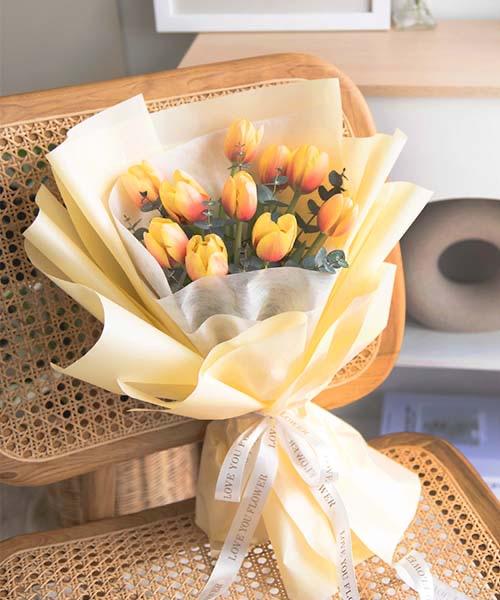 ช่อดอกทิวลิปสีเหลืองส้ม ห่อกระดาษสีครีม วางบนเก้าอี้หวาย