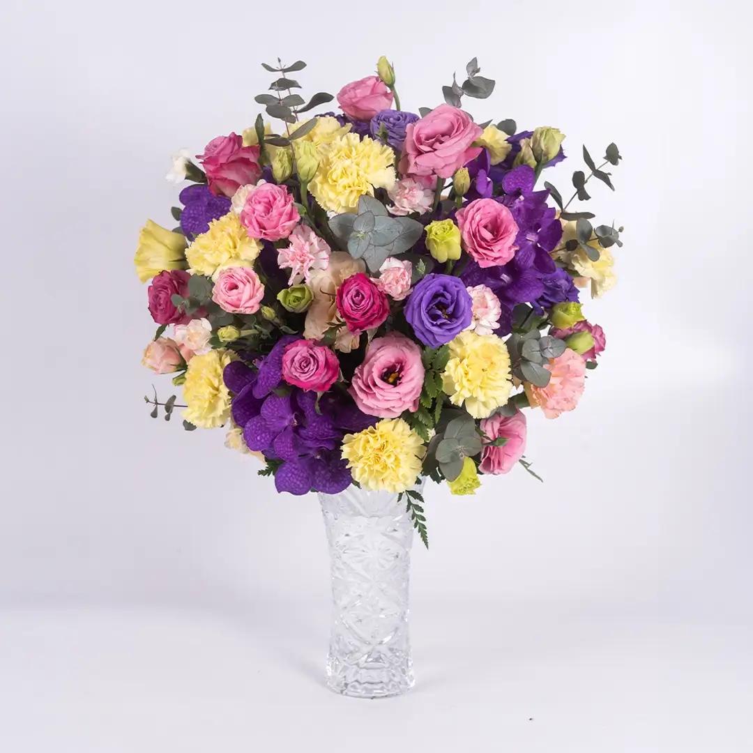 แจกันดอกไลเซนทัส ประกอบไปด้วยดอกกุหลาบ ดอกไลเซนทัส สีม่วง สีพีช และสีชมพู ดอกคาร์เนชัน ดอกกล้วยไม้แวนด้า จัดในแจกันสีใส