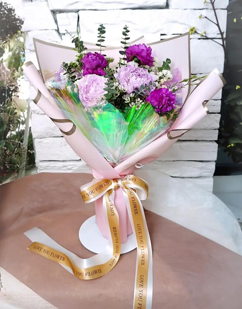 ช่อดอกไม้สดโทนสีม่วงและชมพู ห่อกระดาษสีชมพูอ่อนและกระดาษใสเหลือบสี