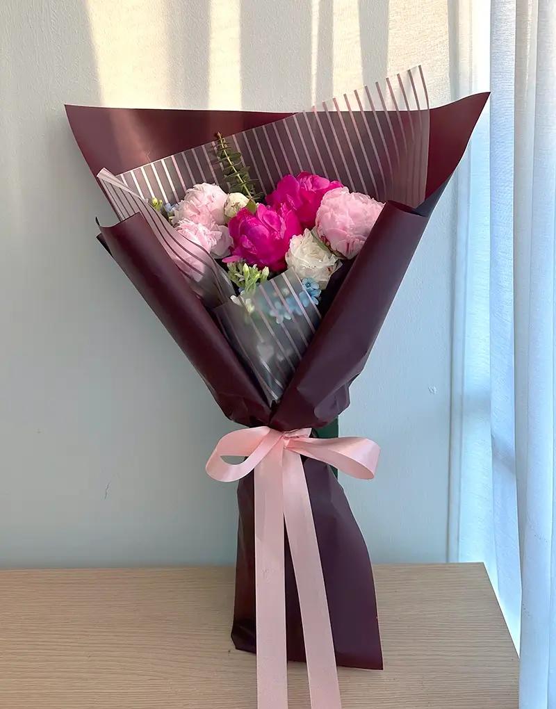 ช่อดอกไม้สดโทนสีชมพูและขาว ห่อกระดาษสีขาวใสผูกริบบิ้นสีชมพูเข้ม