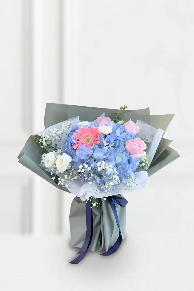 ช่อดอกไม้สดโทนสีฟ้า ชมพู และขาว ห่อกระดาษสีเขียวเทาผูกริบบิ้นสีน้ำเงิน