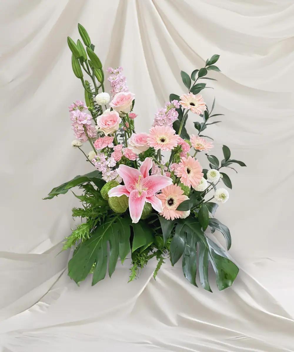 ดอกไม้ประดับโพเดียมโทนสีชมพูและขาว จัดทรงสูงพร้อมใบไม้สีเขียว