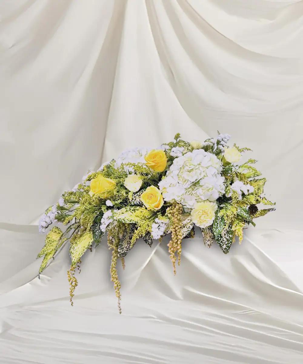 ดอกไม้ประดับโพเดียมโทนสีเหลืองและขาว จัดทรงแนวนอนพร้อมใบไม้สีเขียว