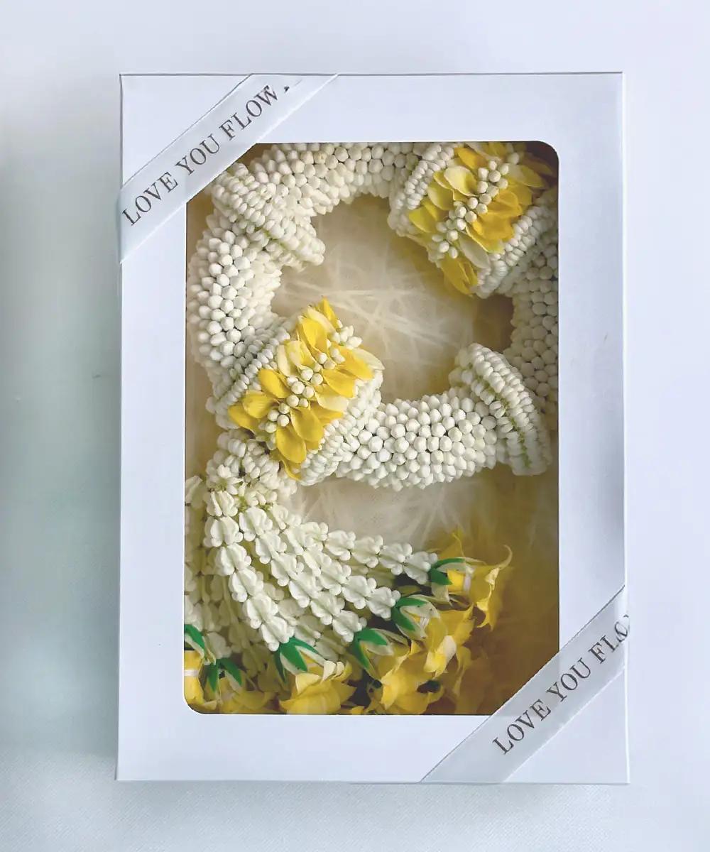 พวงมาลัยดอกมะลิสีขาวตกแต่งดอกสีเหลือง จัดในกล่องสีขาวฝาใส